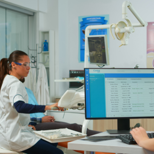 A woman in a white shirt, representing a dental clinic, stands in a healthcare setting, smiling confidently.